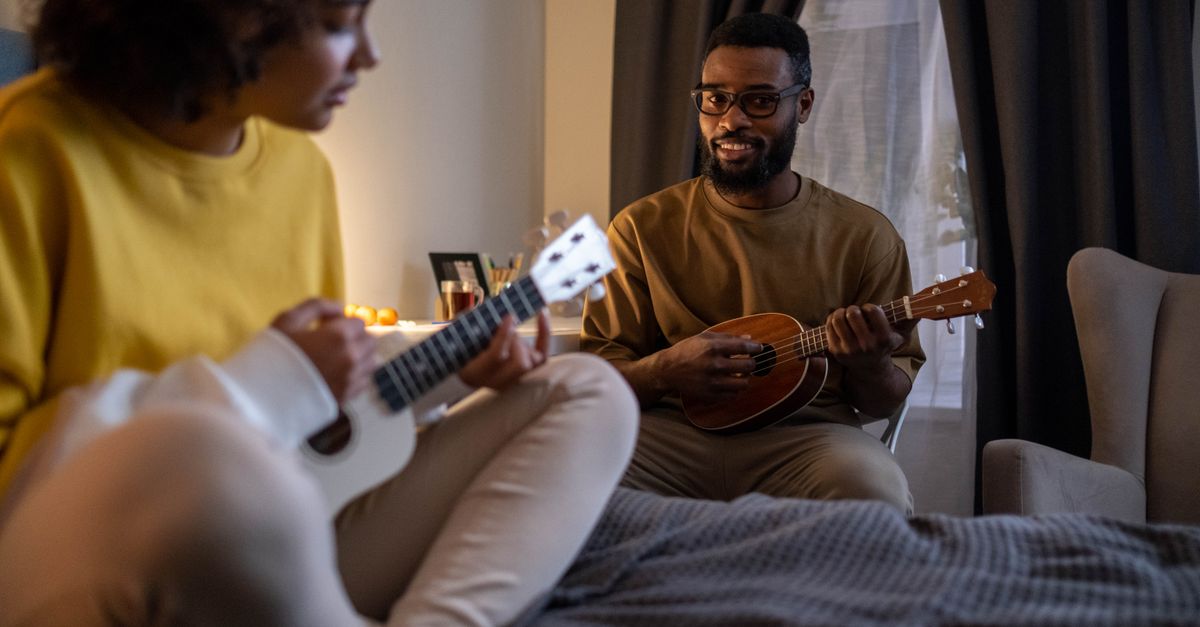 A father and daughter enjoying leisure time playing ukuleles together in a cozy bedroom setting.